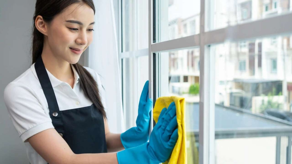 Professional house cleaner wiping window in a Singapore home